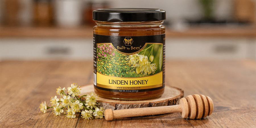 Jar of Linden honey on wooden slice with linden blossoms and a honey dipper on rustic table