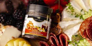 Jar of raw orange blossom honey surrounded by cheese, cured meats, figs, pear slices, and blackberries