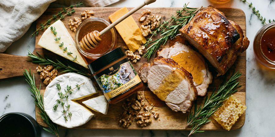 Charcuterie board with roasted pork, cheeses, walnuts, herbs and eucalyptus honey jar with honeycomb
