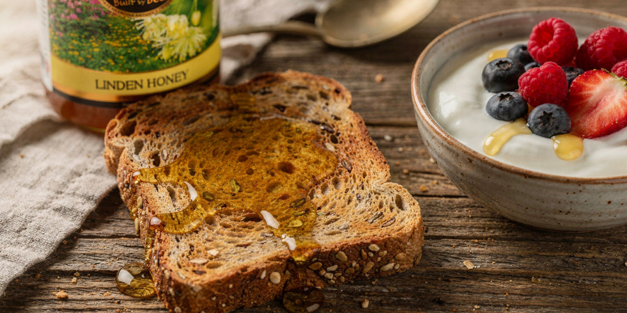 Toasted multigrain bread drizzled with linden honey beside a bowl of yogurt topped with strawberries, raspberries and blueberries