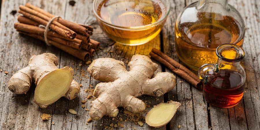 Fresh ginger root and sliced ginger on rustic wood with cinnamon sticks, jar of honey and small vinegar bottle