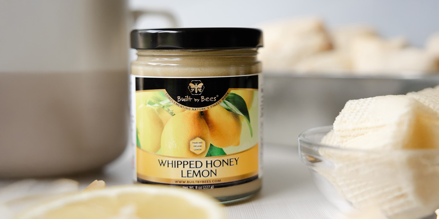Jar of whipped lemon honey on a kitchen table, surrounded by lemon slices and a cup