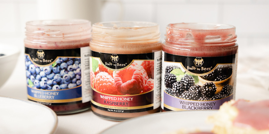Three jars of whipped honey spreads-blueberry, raspberry, and blackberry-on a white countertop